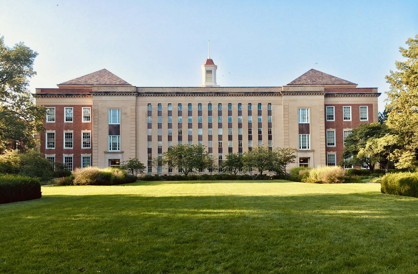 Red-brick campus building behind a green lawn and trees